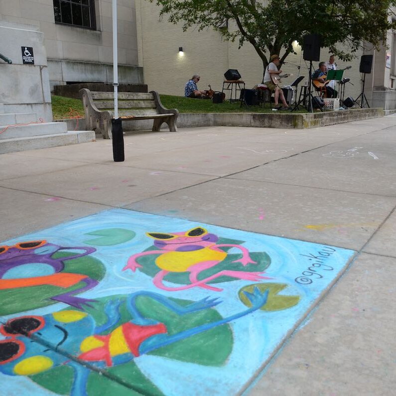 cartoon frogs on lily pad side walk chalk art with live music being played in background in downtown Lewisburg