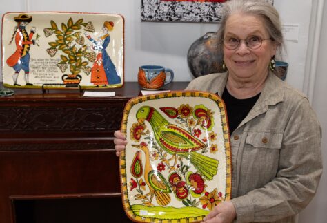 Artist Selinda Kennedy posing with redware platter featuring the design of a folk art parrot and flowers in green and red colors